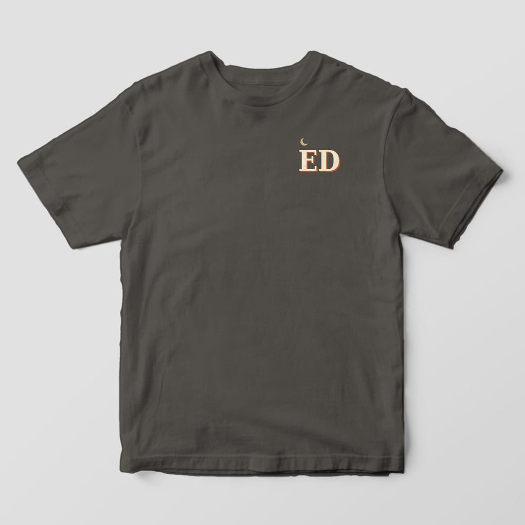 Front of a Pepper Comfort Colors 1717 tee with a small left-chest gold crescent moon above the letters ED in cream with a rust shadow.