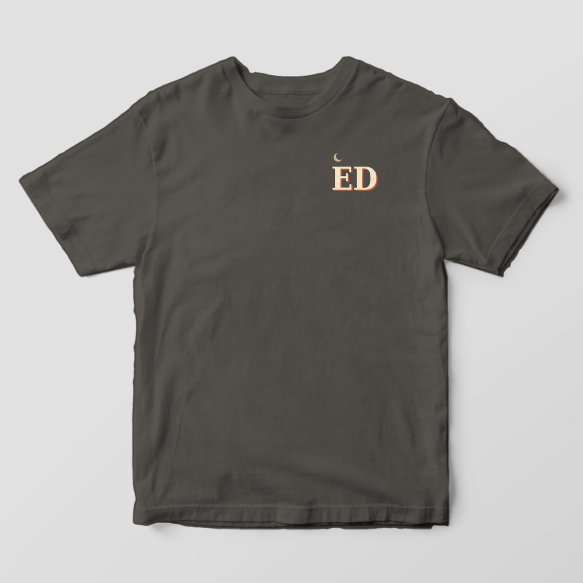 Front of a Pepper Comfort Colors 1717 tee with a small left-chest gold crescent moon above the letters ED in cream with a rust shadow.