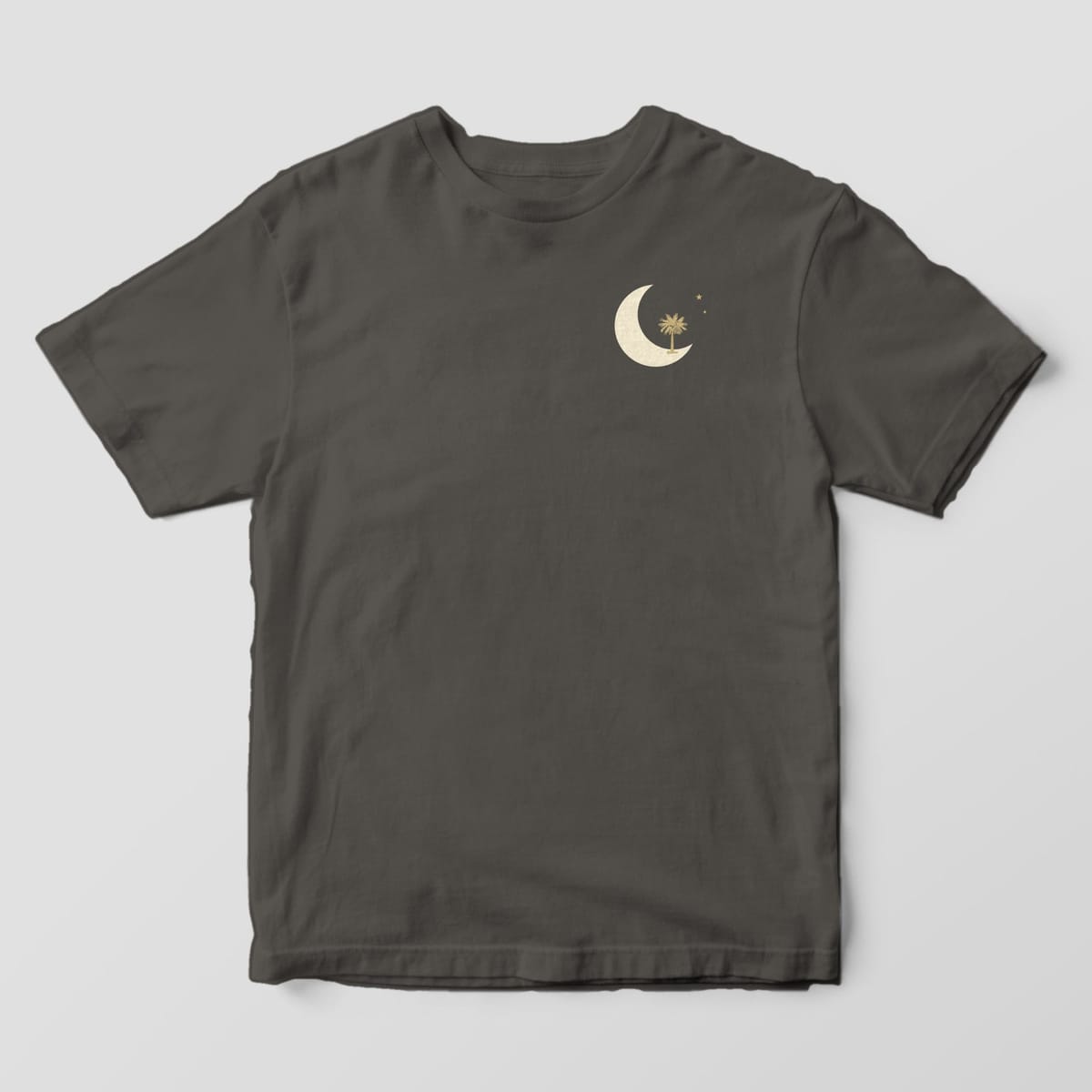 Front of a Pepper Comfort Colors 1717 tee with a small left-chest cream crescent moon with a gold palmetto tree and two stars.