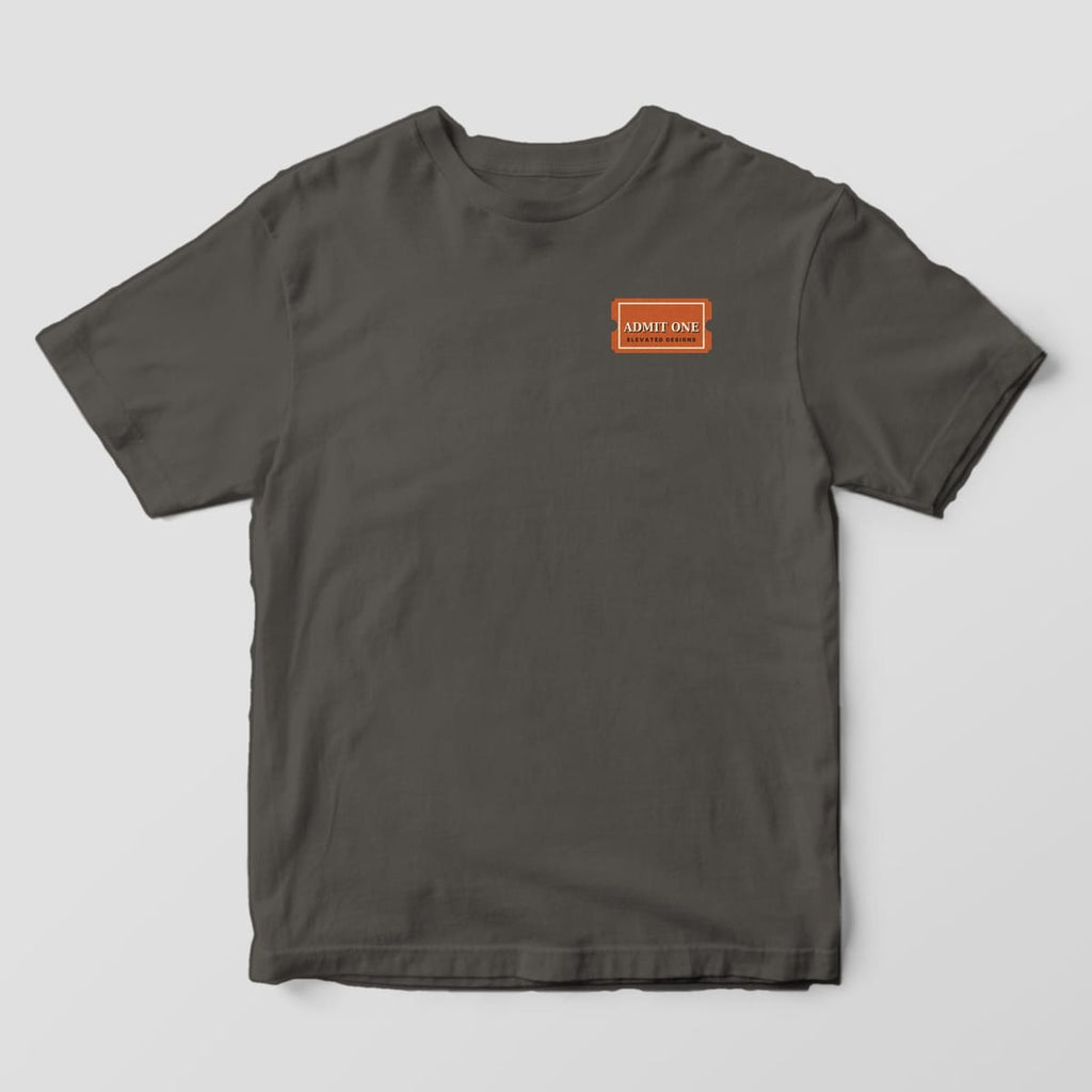 Front of a Pepper Comfort Colors 1717 tee with a small left-chest rust ticket stub reading ADMIT ONE, ELEVATED DESIGNS.