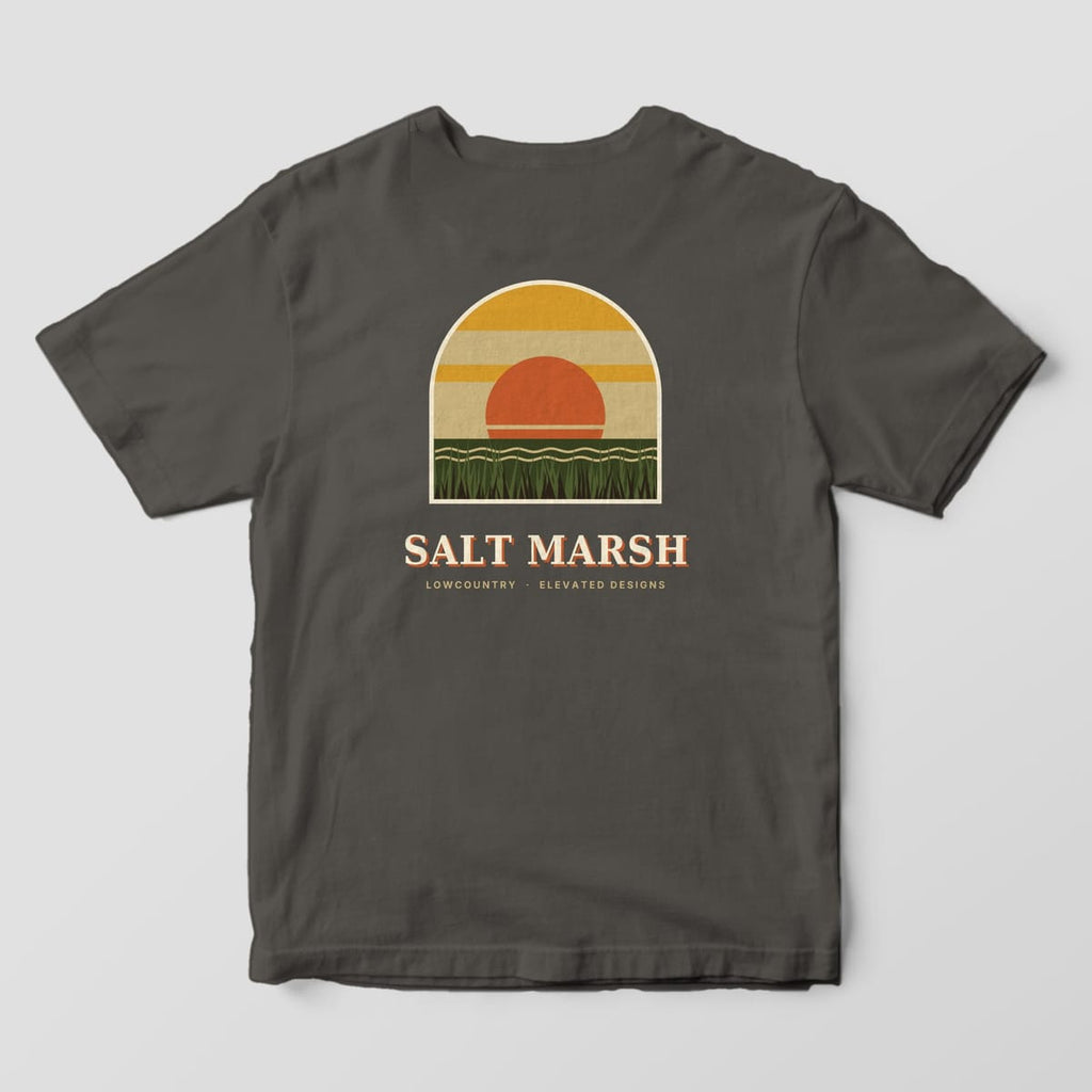 Back of a Pepper Comfort Colors 1717 tee with an arched window scene of an orange sun setting over wavy water and tall green marsh grass under gold and tan bands, above SALT MARSH and LOWCOUNTRY · ELEVATED DESIGNS.