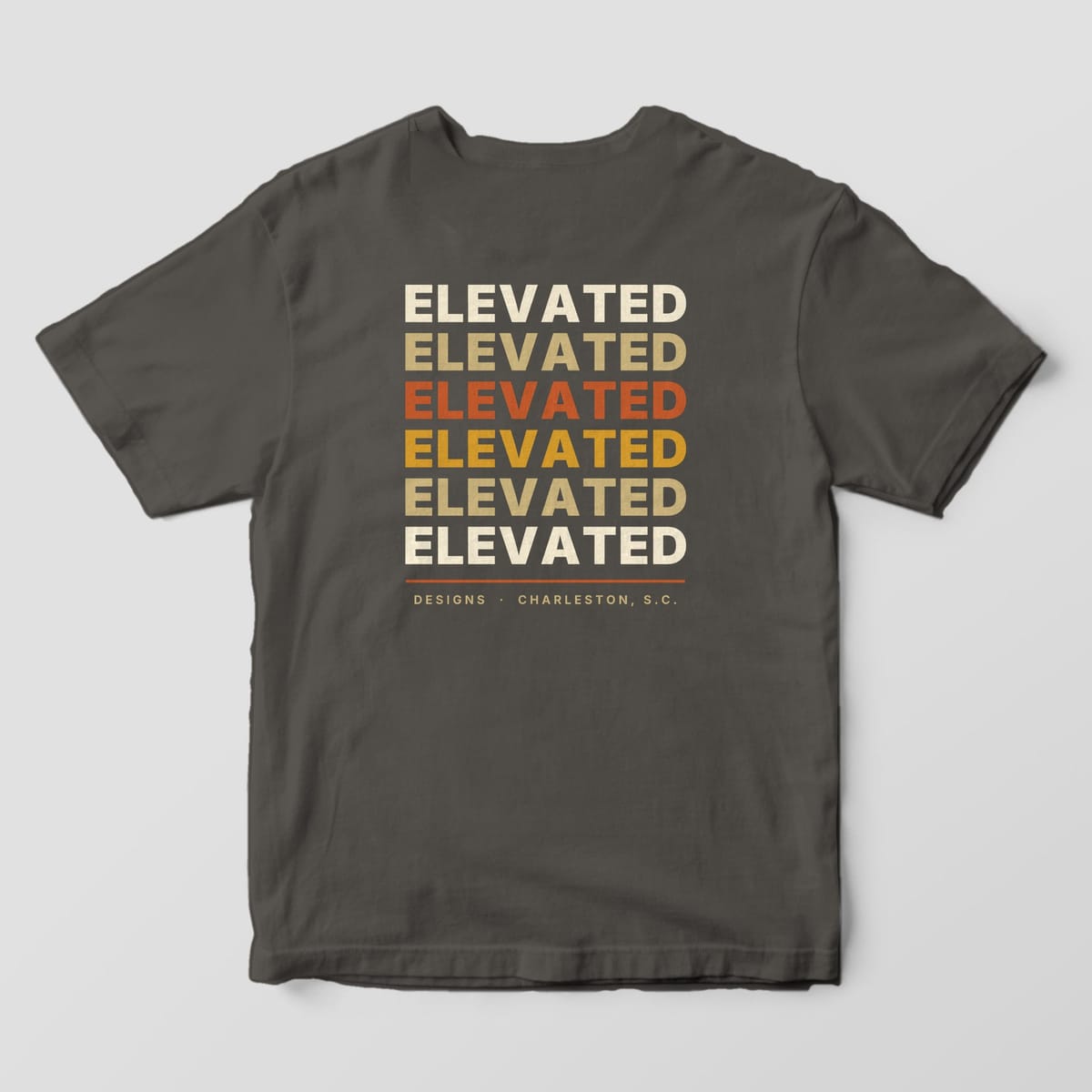 Back of a Pepper Comfort Colors 1717 tee with the word ELEVATED stacked six times in cream, tan, rust, gold, tan and cream, with a rust line and DESIGNS · CHARLESTON, S.C.