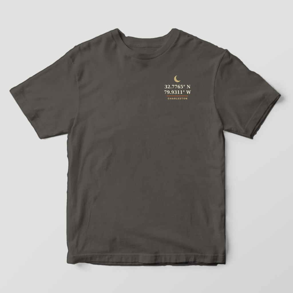 Front of a Pepper Comfort Colors 1717 tee with a small left-chest gold crescent moon above 32.7765° N 79.9311° W and the word CHARLESTON.