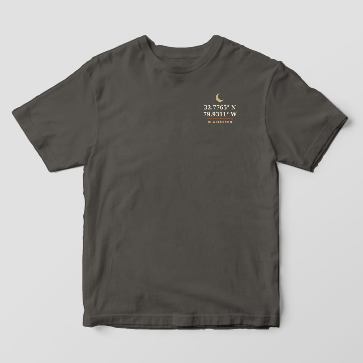Front of a Pepper Comfort Colors 1717 tee with a small left-chest gold crescent moon above 32.7765° N 79.9311° W and the word CHARLESTON.