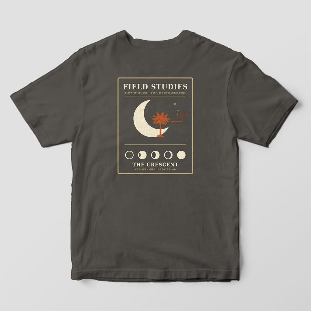 Back of a Pepper Comfort Colors 1717 tee with a tan-outlined Field Studies card with a cream crescent moon, a rust palmetto, a FIG. 02 callout, five moon phases and THE CRESCENT, AS FLOWN ON THE STATE FLAG.