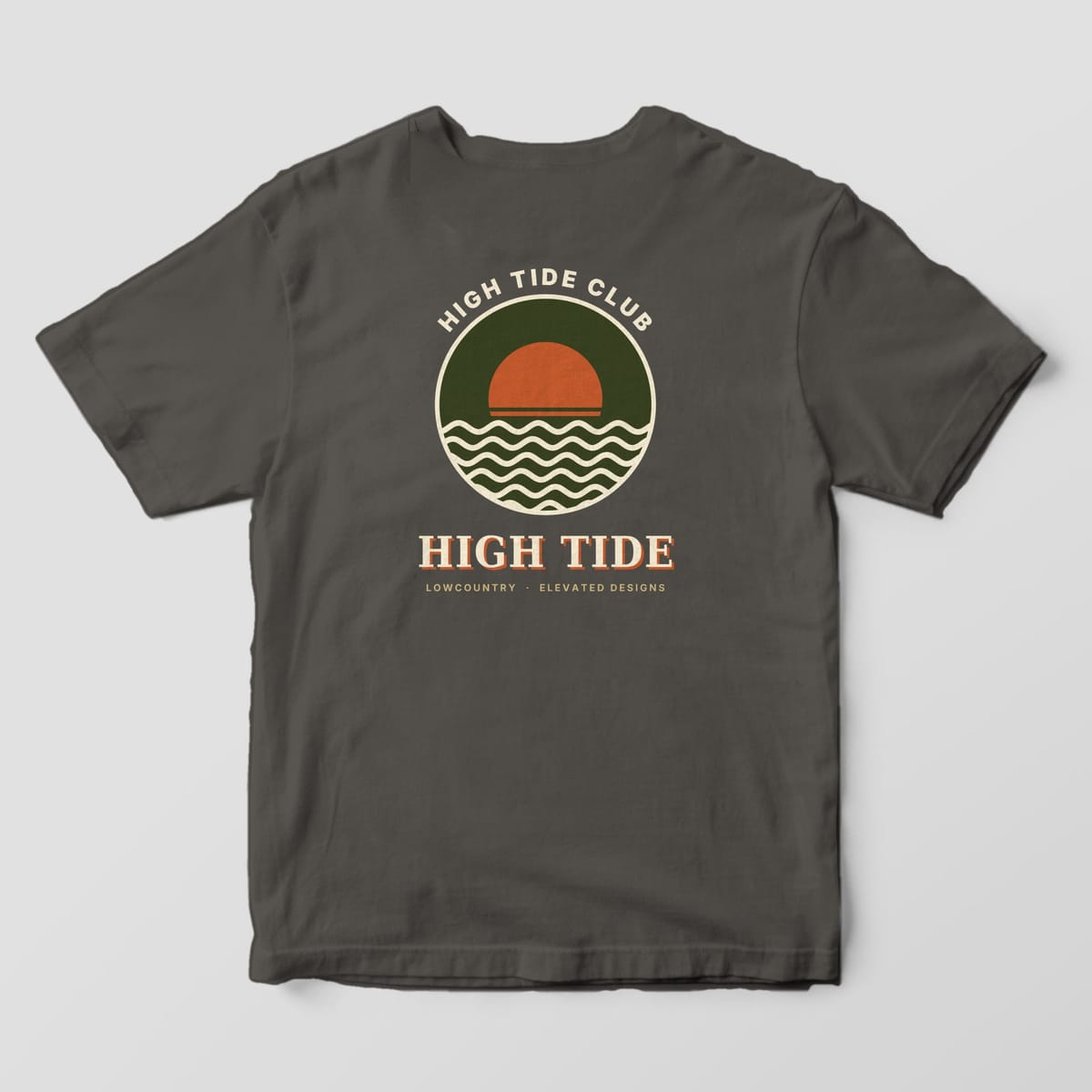 Back of a Pepper Comfort Colors 1717 tee with HIGH TIDE CLUB arched over a round olive badge with a rust sun and cream waves, above HIGH TIDE and LOWCOUNTRY · ELEVATED DESIGNS.