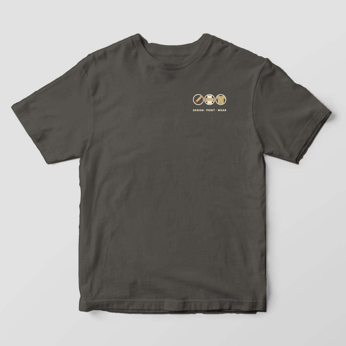 Front of a Pepper Comfort Colors 1717 tee with a small left-chest row of a pencil, printer and t-shirt icon in cream circles above DESIGN · PRINT · WEAR.