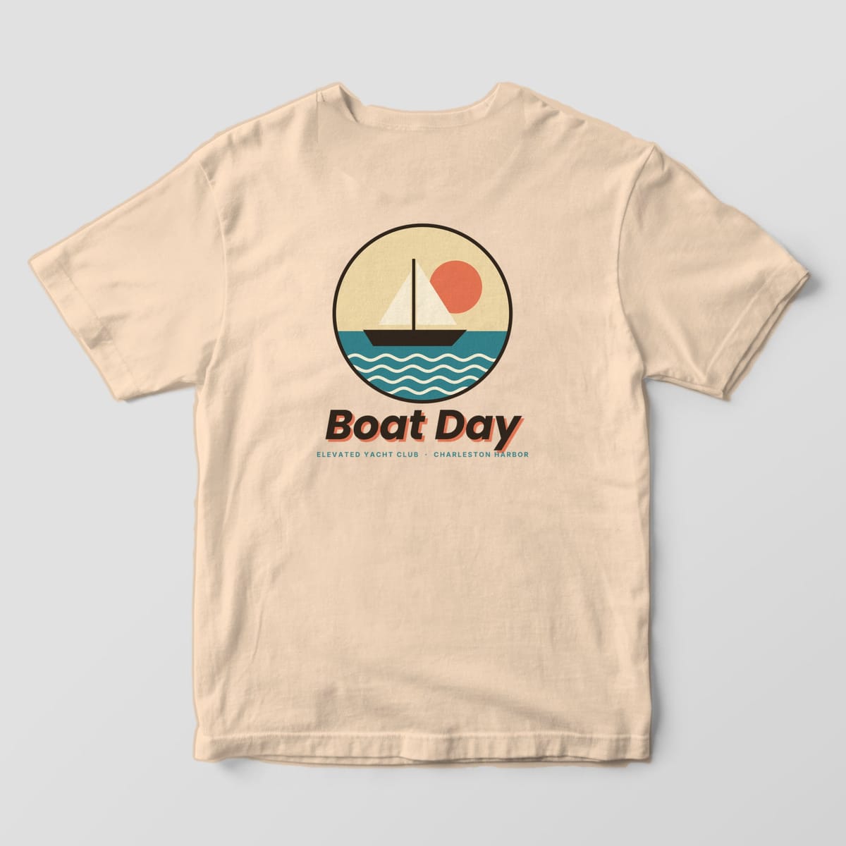 Back of an Ivory Comfort Colors 1717 tee with a round badge of a sailboat on teal water under a coral sun, above Boat Day and ELEVATED YACHT CLUB · CHARLESTON HARBOR.