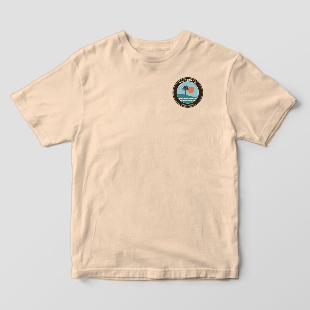 Front of an Ivory Comfort Colors 1717 tee with a small left-chest round badge reading SURF CHECK and FOLLY BEACH around a palmetto, sun and waves.
