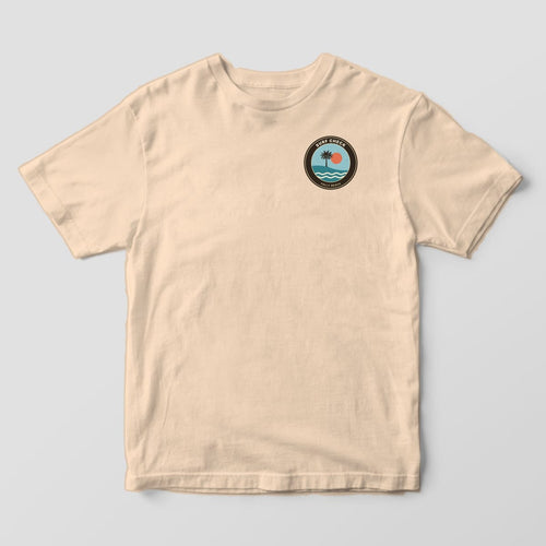 Front of an Ivory Comfort Colors 1717 tee with a small left-chest round badge reading SURF CHECK and FOLLY BEACH around a palmetto, sun and waves.