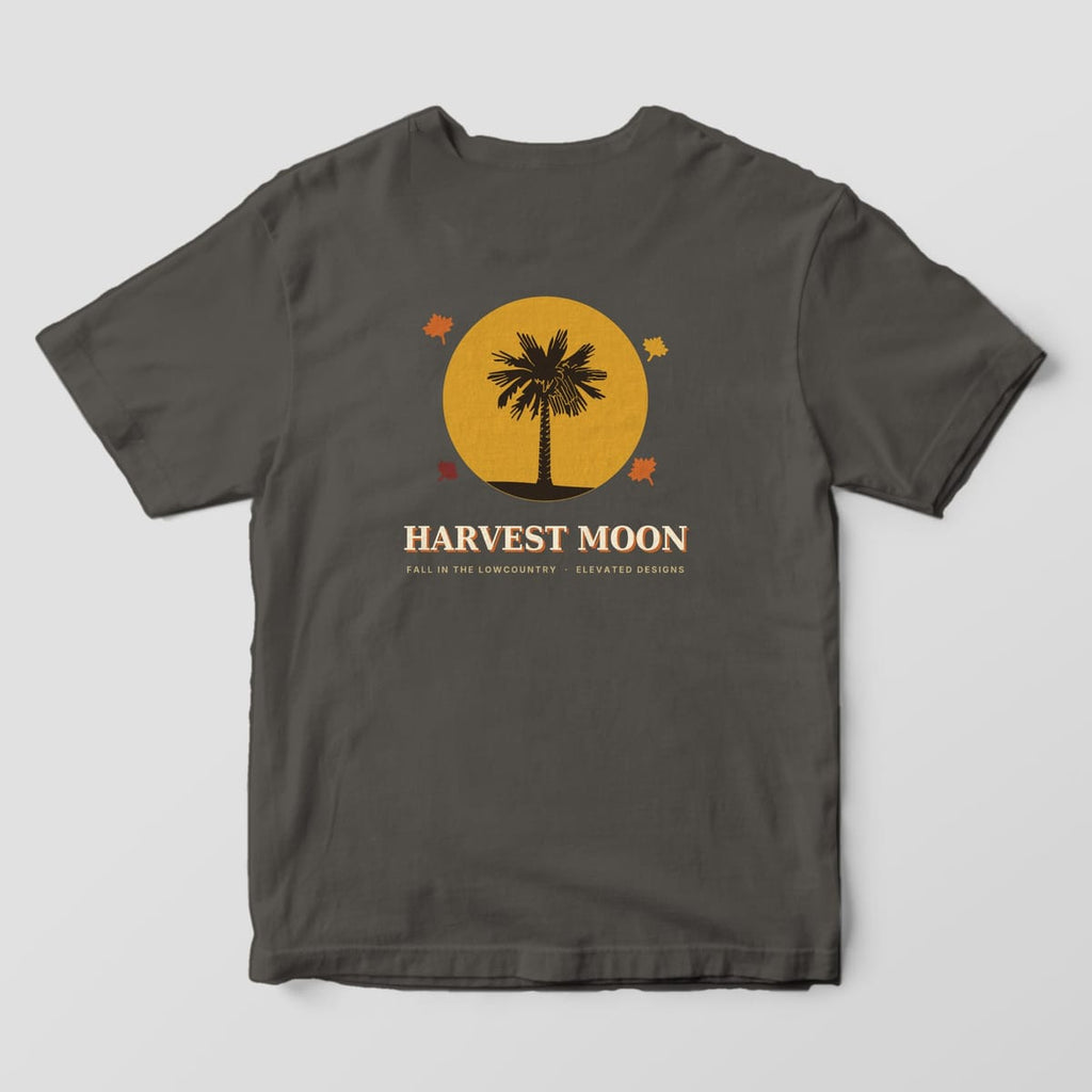 Back of a Pepper Comfort Colors 1717 tee with a dark palmetto silhouette in front of a large gold moon with four autumn leaves, above HARVEST MOON and FALL IN THE LOWCOUNTRY · ELEVATED DESIGNS.