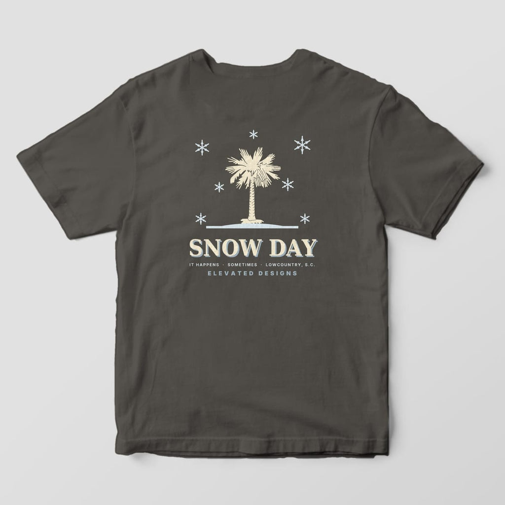 Back of a Pepper Comfort Colors 1717 tee with a cream palmetto on a pale blue snow line surrounded by snowflakes, above SNOW DAY and IT HAPPENS · SOMETIMES · LOWCOUNTRY, S.C.