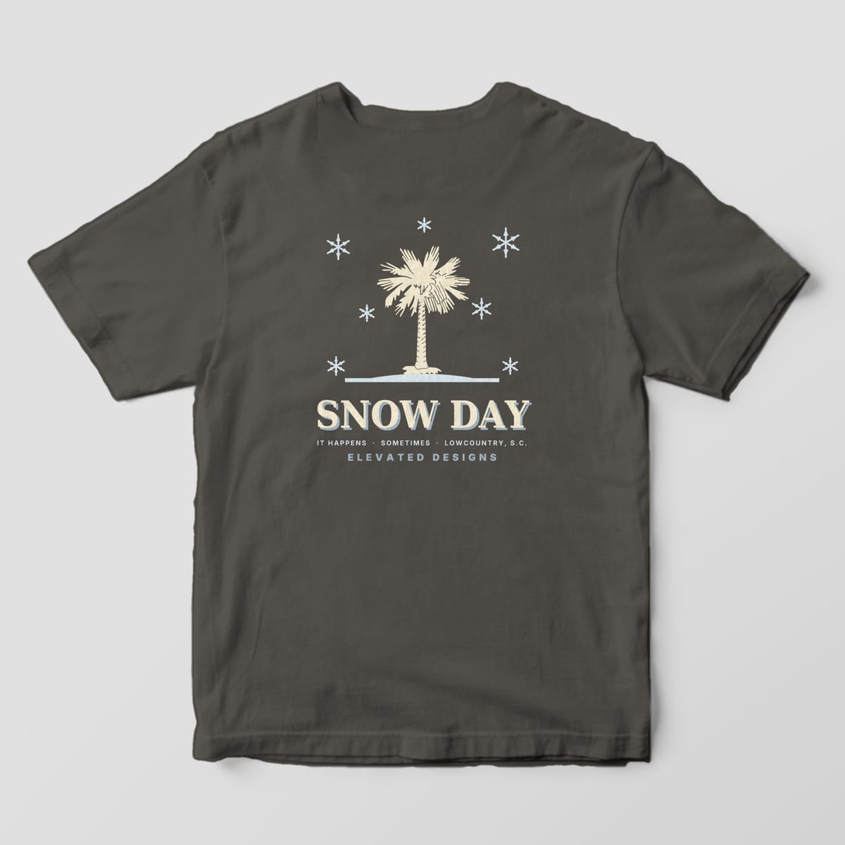 Back of a Pepper Comfort Colors 1717 tee with a cream palmetto on a pale blue snow line surrounded by snowflakes, above SNOW DAY and IT HAPPENS · SOMETIMES · LOWCOUNTRY, S.C.
