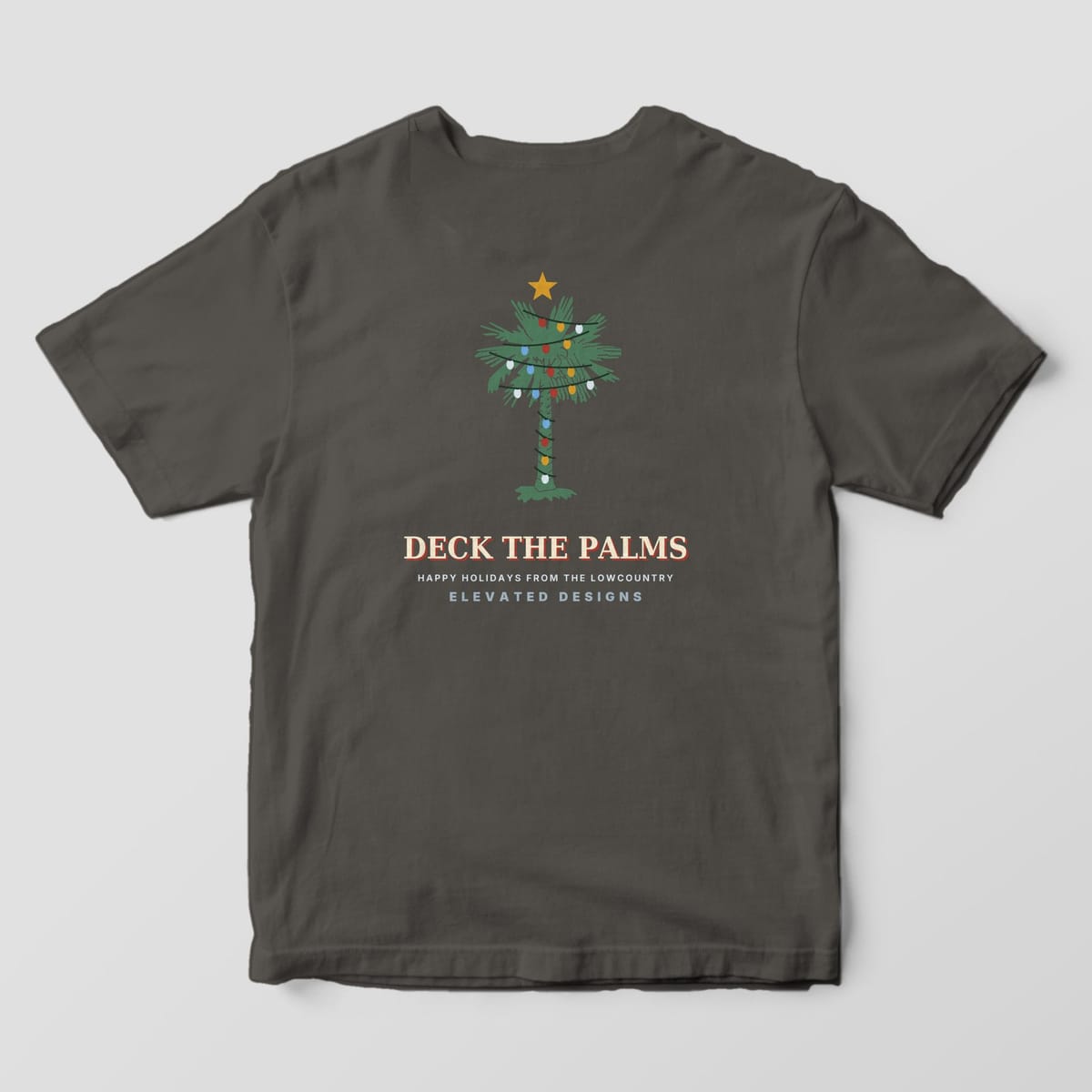 Back of a Pepper Comfort Colors 1717 tee with a green palmetto wrapped in red, gold, blue and white Christmas lights with a gold star on top, above DECK THE PALMS and HAPPY HOLIDAYS FROM THE LOWCOUNTRY.