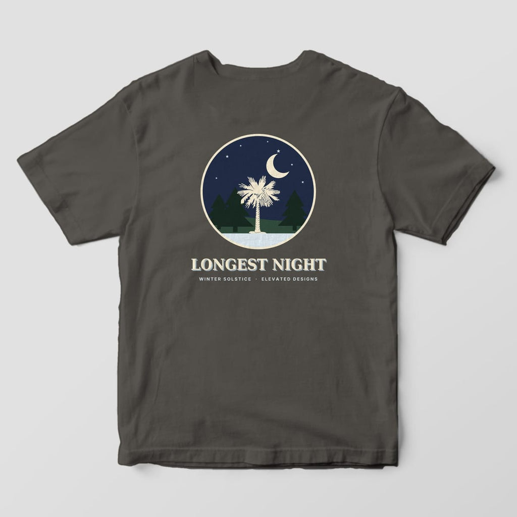 Back of a Pepper Comfort Colors 1717 tee with a round navy night scene of a cream palmetto between dark pine trees under a crescent moon and stars, above LONGEST NIGHT and WINTER SOLSTICE · ELEVATED DESIGNS.