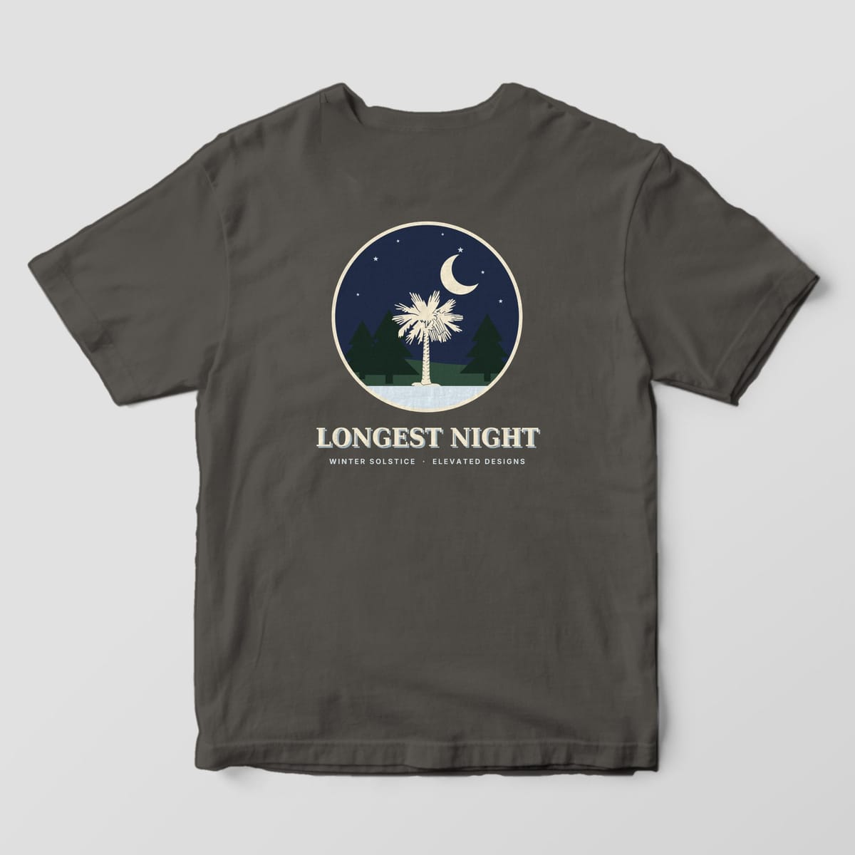 Back of a Pepper Comfort Colors 1717 tee with a round navy night scene of a cream palmetto between dark pine trees under a crescent moon and stars, above LONGEST NIGHT and WINTER SOLSTICE · ELEVATED DESIGNS.