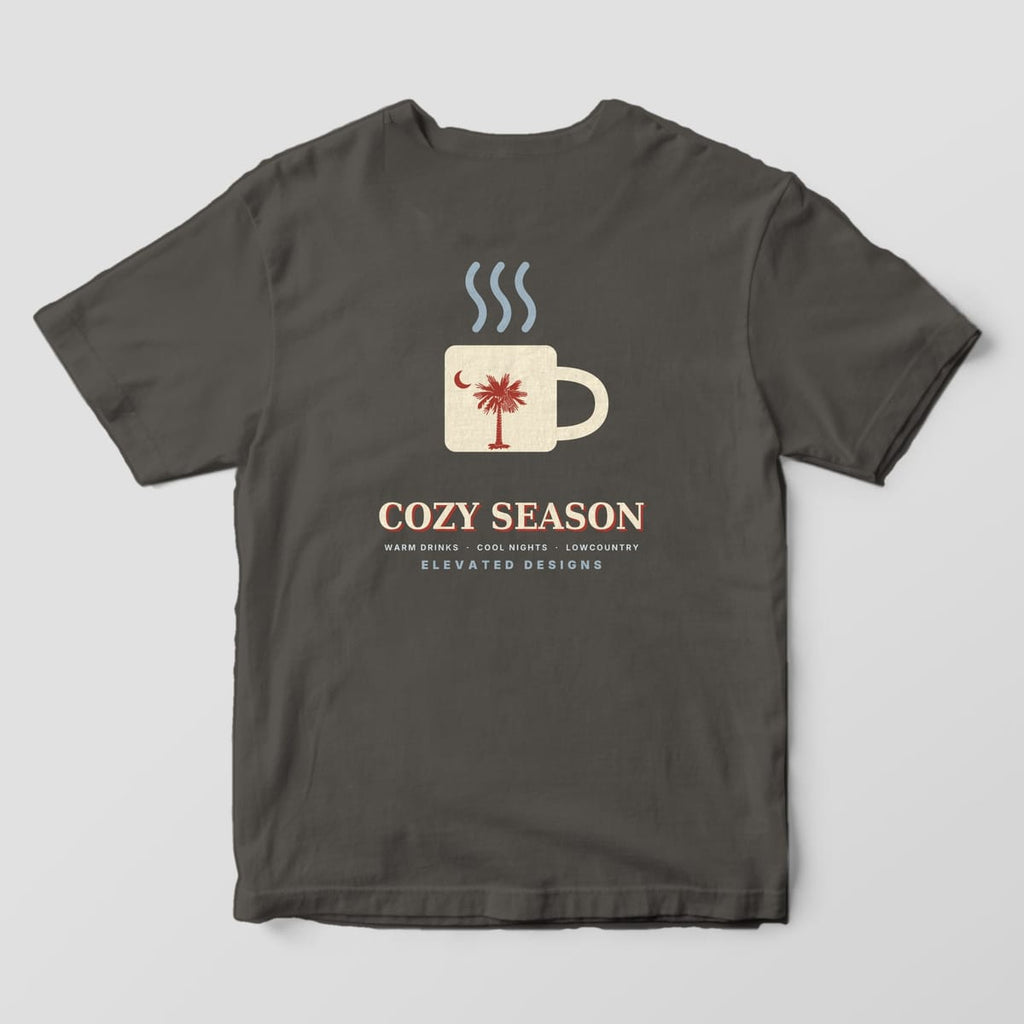 Back of a Pepper Comfort Colors 1717 tee with a cream mug with a red palmetto and crescent moon under three steam lines, above COZY SEASON and WARM DRINKS · COOL NIGHTS · LOWCOUNTRY.