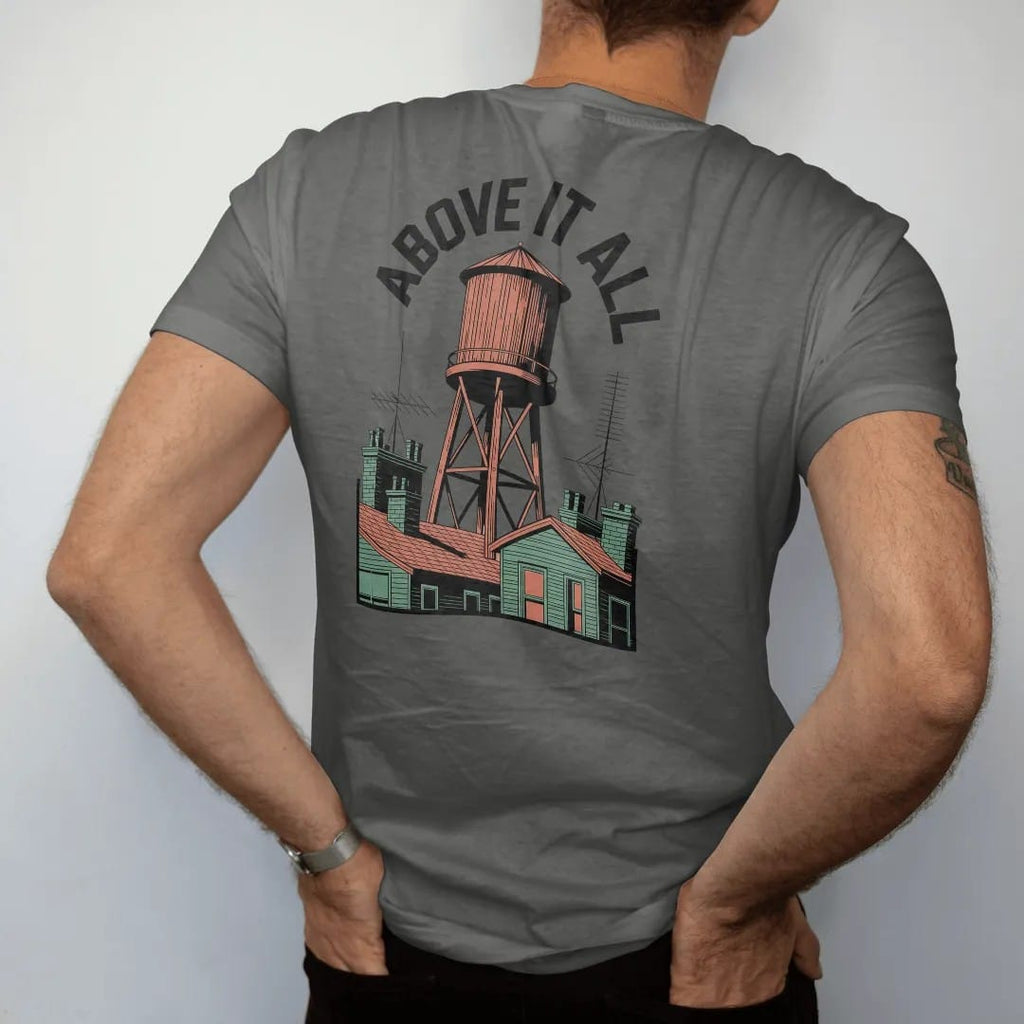 Man wearing a Pepper tee, seen from the back: a wooden rooftop water tower over brownstone roofs with Above It All arched across the top in bone white, orange and green.