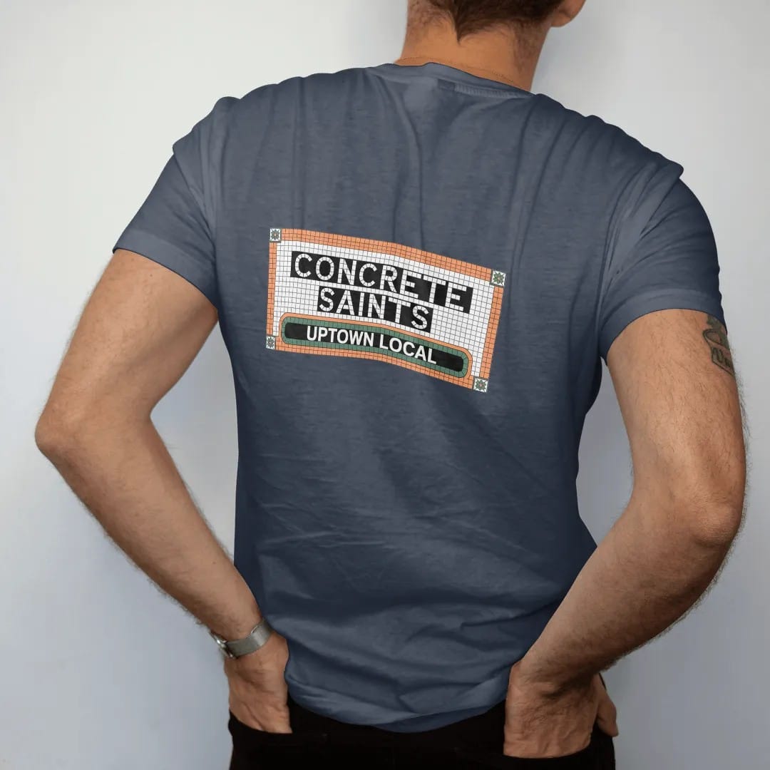 Man wearing a Midnight tee, seen from the back: a subway-style mosaic tile name tablet spelling Concrete Saints over a smaller Uptown Local band, in bone white, green, orange and yellow tiles.