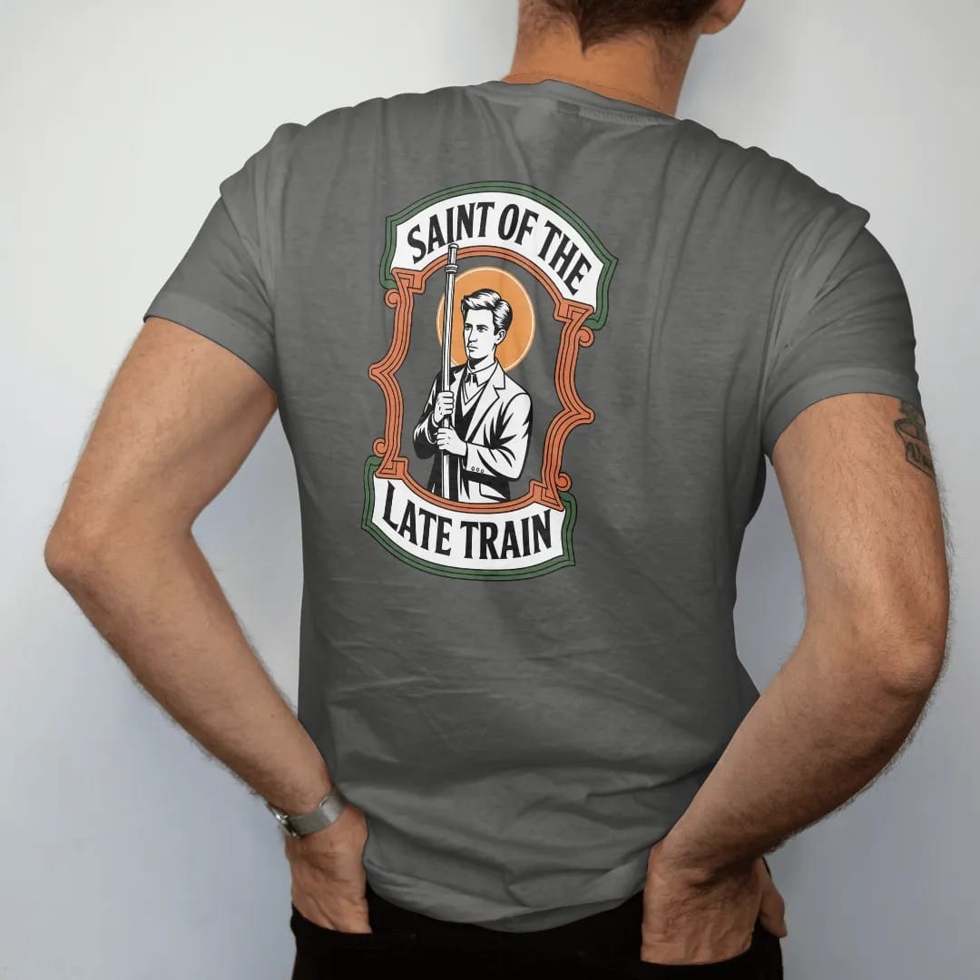 Man wearing a Pepper tee, seen from the back: a prayer-candle style label of a haloed commuter holding a subway pole, titled Saint Of The Late Train, in bone white, yellow, orange and green.