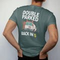Man wearing a Blue Spruce tee, seen from the back: the back of a van with blinking hazard lights under Double Parked and a scribbled Back In 5 note, in orange, yellow, bone white and green.