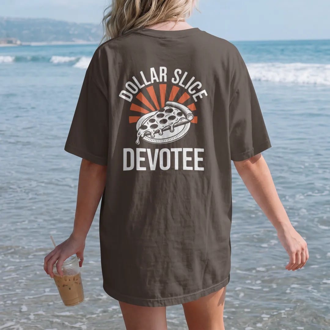 Woman on the beach in a Espresso tee, back view: a dripping pizza slice on a paper plate with holy rays under Dollar Slice and over Devotee, in yellow, orange, bone white and green.
