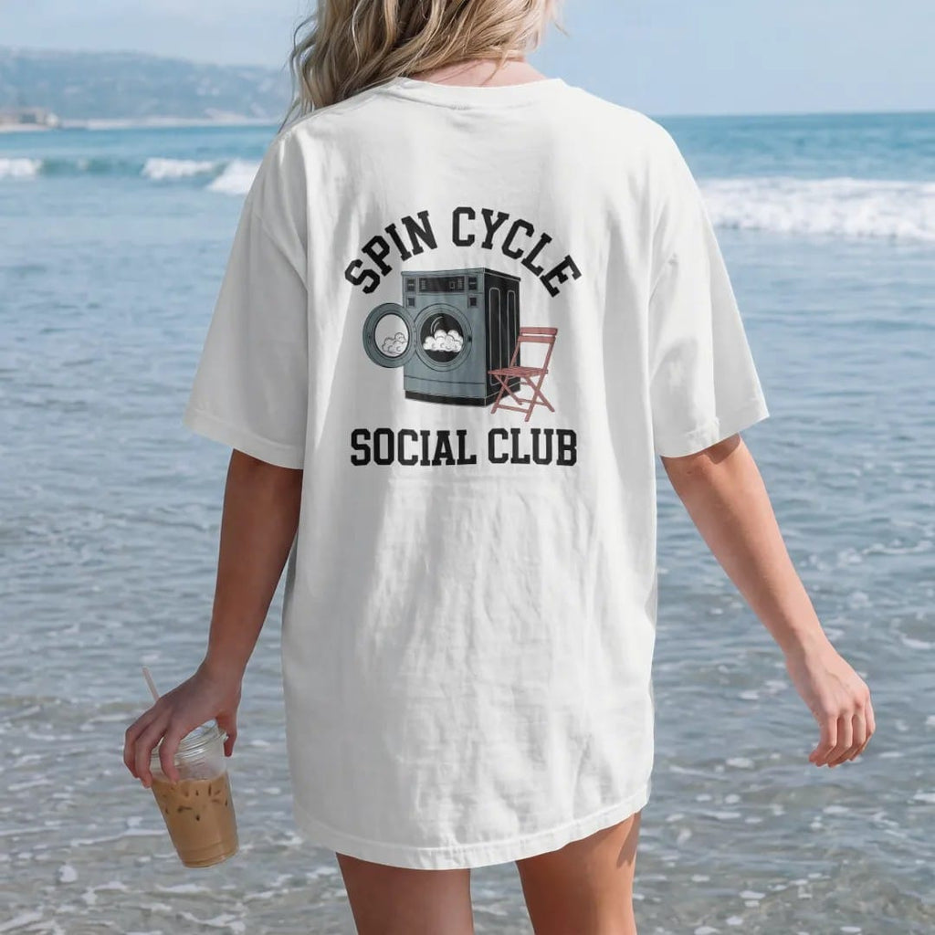 Woman on the beach in a White tee, back view: a retro laundromat washer with spinning suds and a folding chair under Spin Cycle and over Social Club, in charcoal, brick red, green and navy.