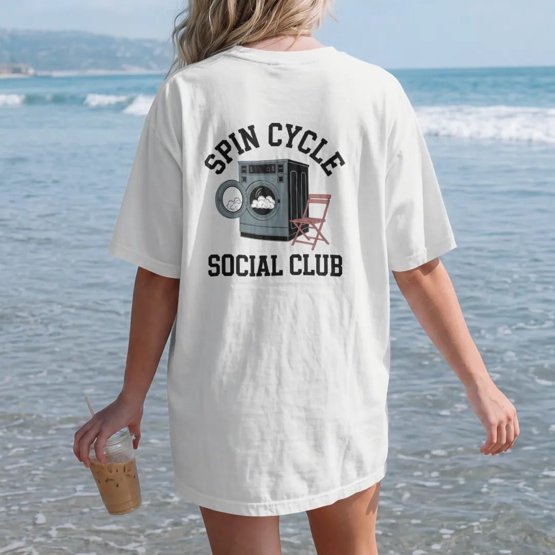 Woman on the beach in a White tee, back view: a retro laundromat washer with spinning suds and a folding chair under Spin Cycle and over Social Club, in charcoal, brick red, green and navy.