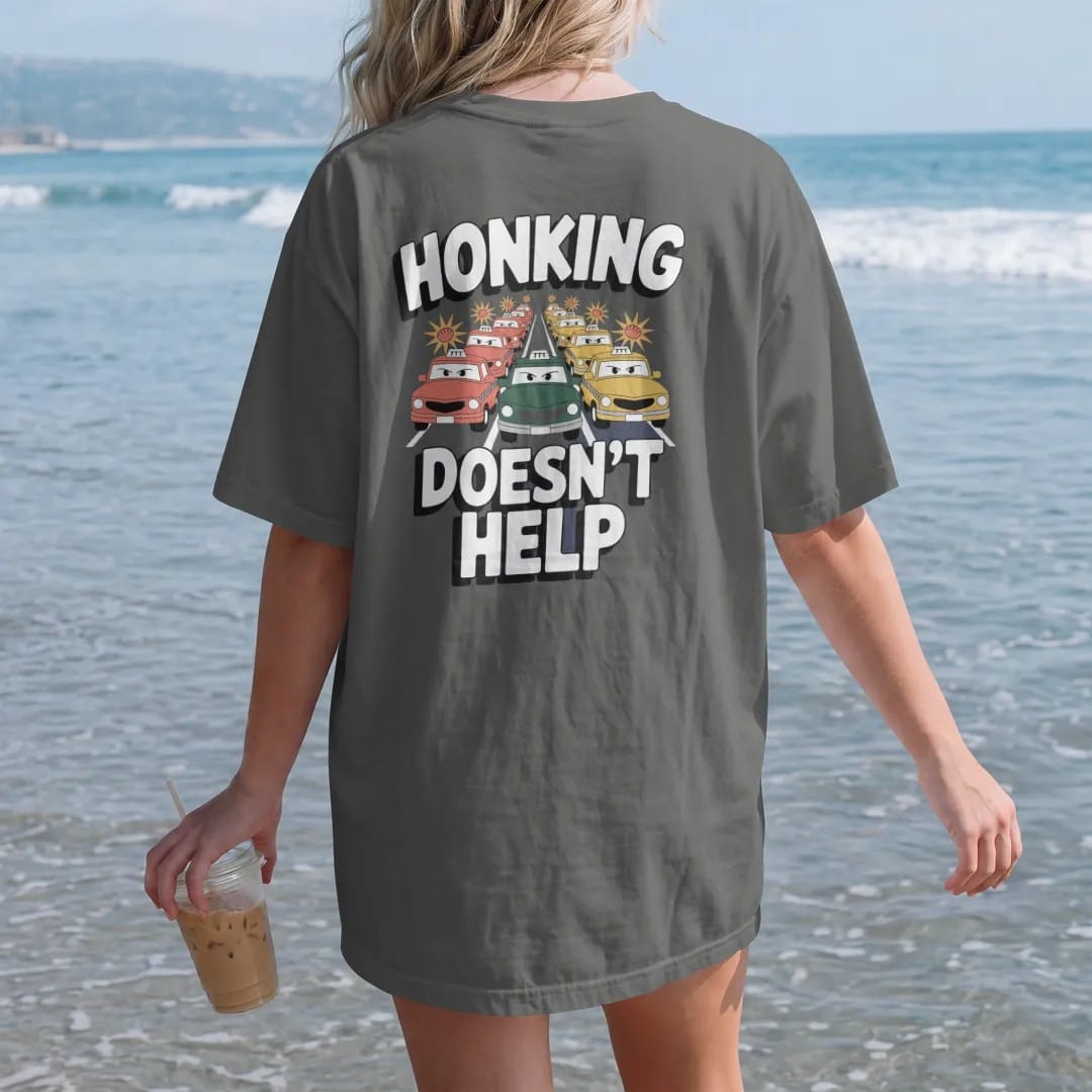 Woman on the beach in a Pepper tee, back view: a cartoon traffic jam of taxis and buses with horn bursts under Honking and calm Doesn't Help lettering, in yellow, orange, bone white and green.