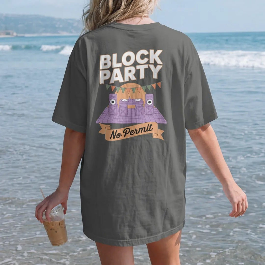 Woman on the beach in a Pepper tee, back view: a DJ table on milk crates with speakers and paper flags along a brownstone block, under Block Party and a No Permit ribbon, in orange, yellow, bone white and green.