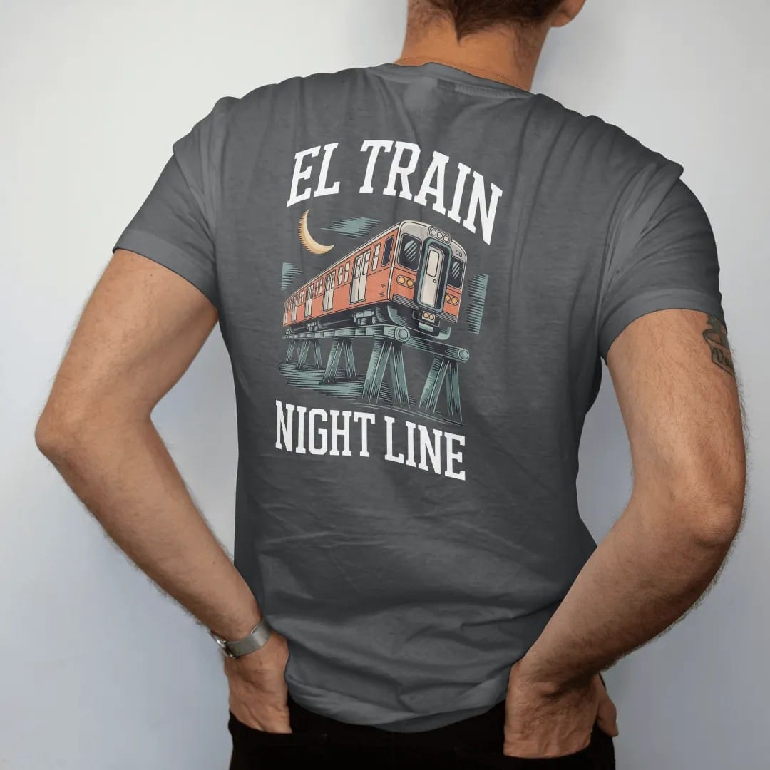 Man wearing a Graphite tee, seen from the back: an elevated train with lit windows crossing steel trestles under a crescent moon, with El Train above and Night Line below, in yellow, bone white, orange and green.