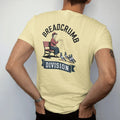 Man wearing a Butter tee, seen from the back: an older woman on a park bench tossing crumbs to pigeons under Breadcrumb arched over a Division ribbon, in charcoal, brick red, green and navy.