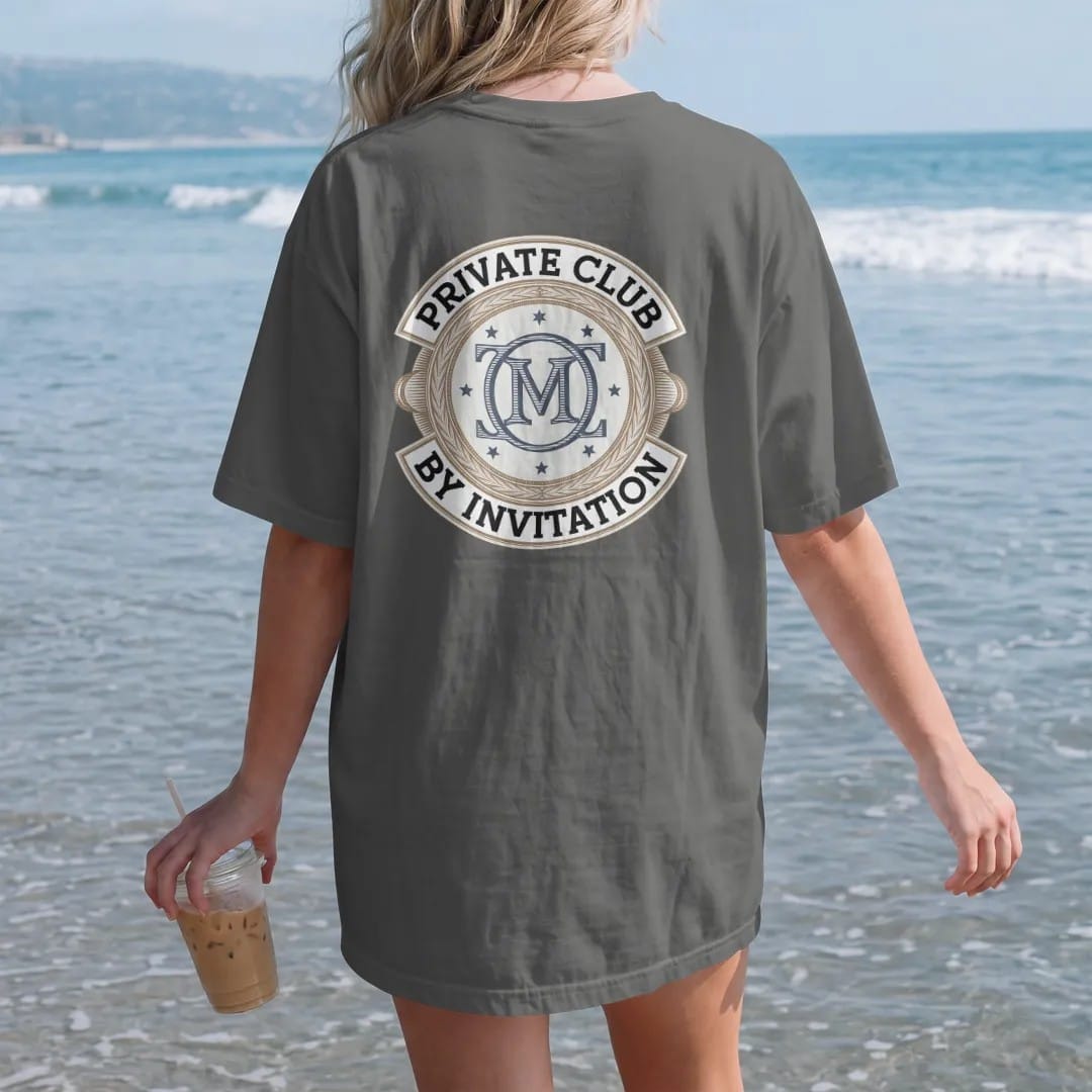Woman on the beach in a Pepper tee, back view: an interlocking serif monogram in a double ring with tiny stars, ringed by Private Club and By Invitation, as a fine engraving in navy and antique gold.