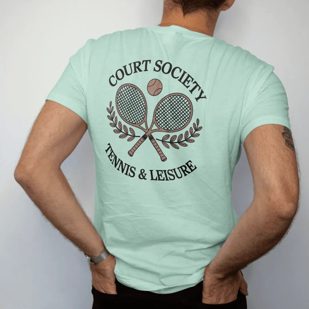 Man wearing a Chalky Mint tee, seen from the back: two crossed wooden tennis rackets with a ball and laurel sprigs under Court Society and Tennis & Leisure, as a fine engraving in navy and antique gold.