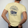 Man wearing a Butter tee, seen from the back: a vintage convertible with a picnic basket and umbrella in a round emblem, ringed by Weekend Society and Since Friday, as a fine engraving in navy and antique gold.