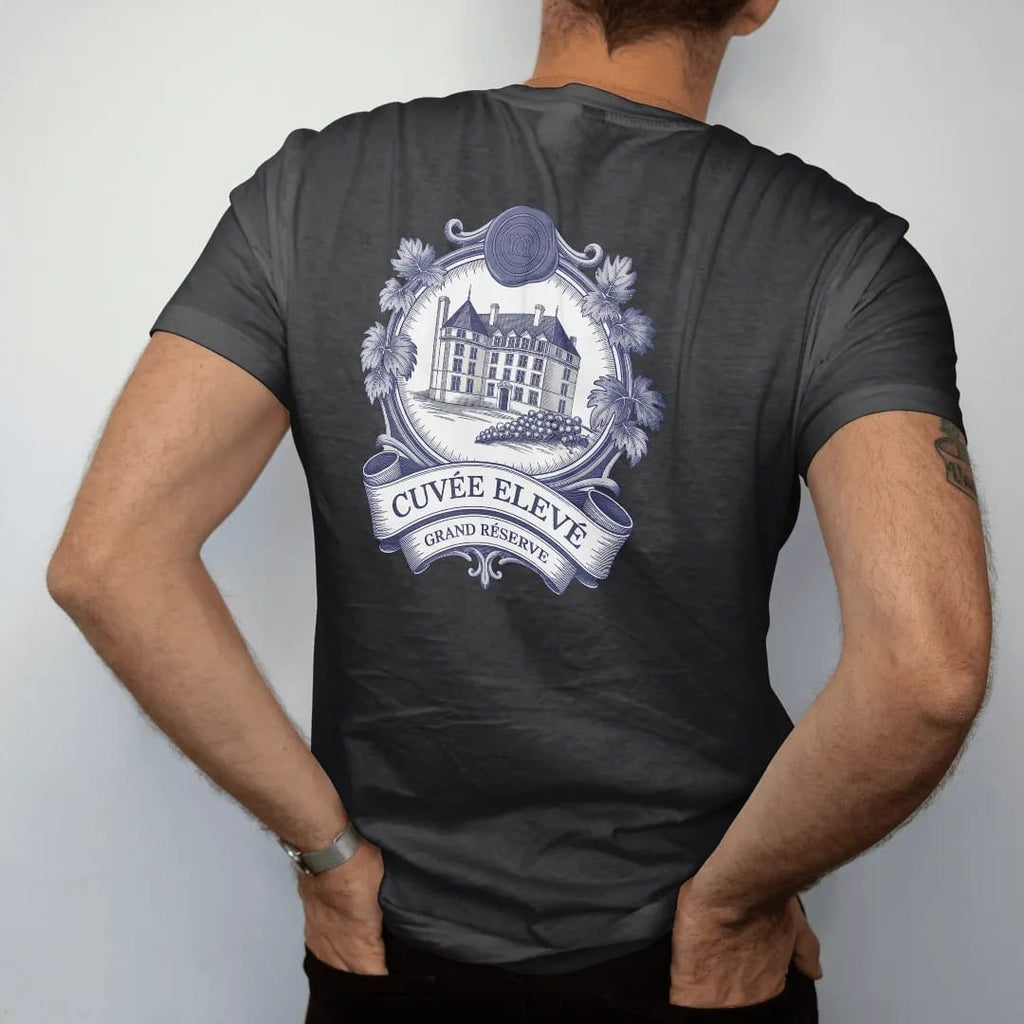 Man wearing a Black tee, seen from the back: a vintage wine label with an engraved château, grapevines and a wax seal, reading Cuvée Elevé with a Grand Réserve banner, as a fine engraving in navy and antique gold.