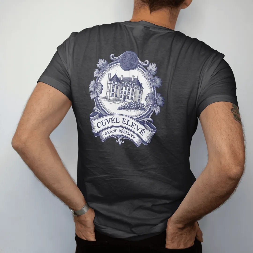 Man wearing a Black tee, seen from the back: a vintage wine label with an engraved château, grapevines and a wax seal, reading Cuvée Elevé with a Grand Réserve banner, as a fine engraving in navy and antique gold.