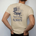 Man wearing a Sandstone tee, seen from the back: overlapping vintage passport stamps and a ticket with a propeller plane, under First Class in serif and Always, as a fine engraving in navy and antique gold.