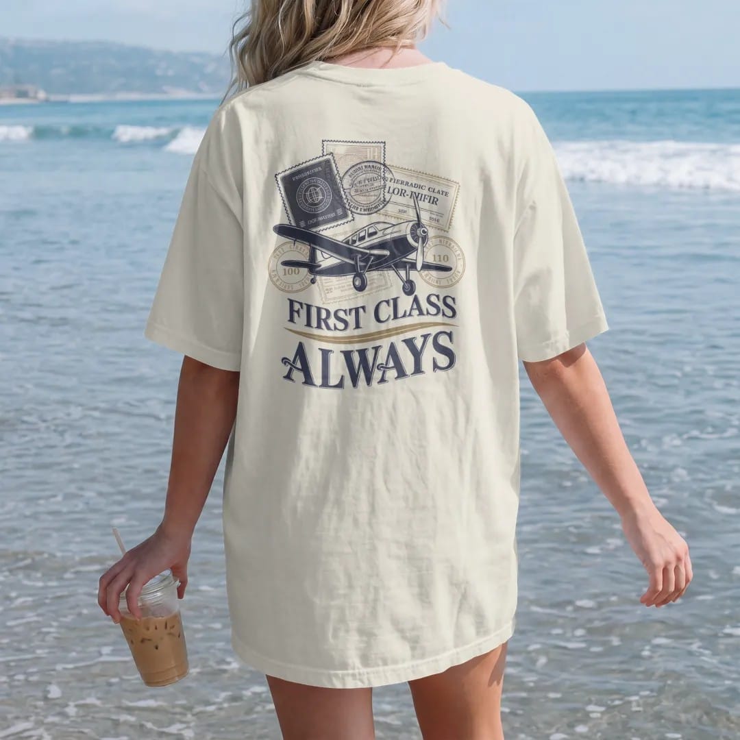 Woman on the beach in a Ivory tee, back view: overlapping vintage passport stamps and a ticket with a propeller plane, under First Class in serif and Always, as a fine engraving in navy and antique gold.