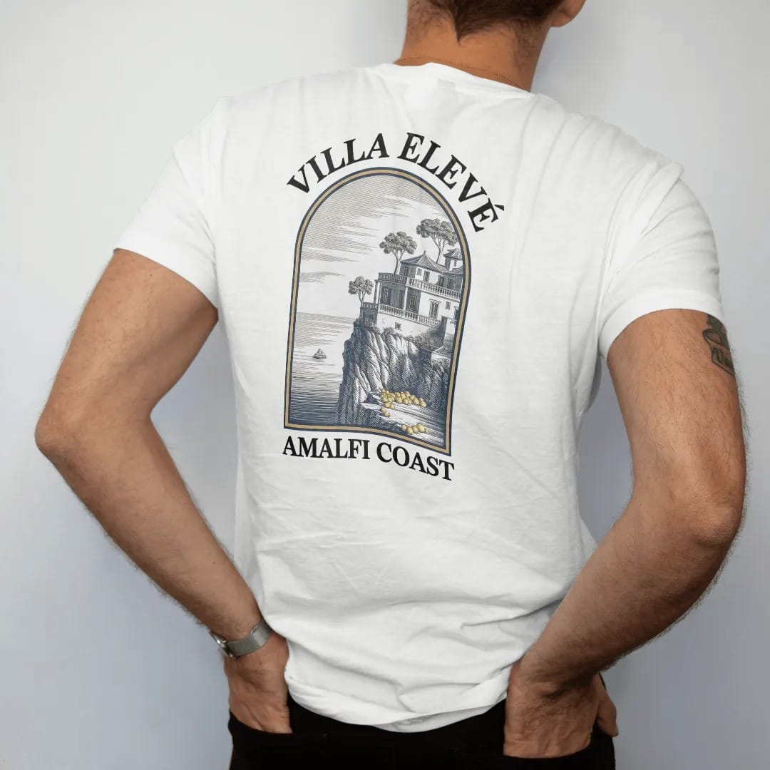 Man wearing a White tee, seen from the back: a cliffside villa with lemon terraces above the sea in an arched frame, under Villa Elevé and Amalfi Coast, as a fine engraving in navy and antique gold.