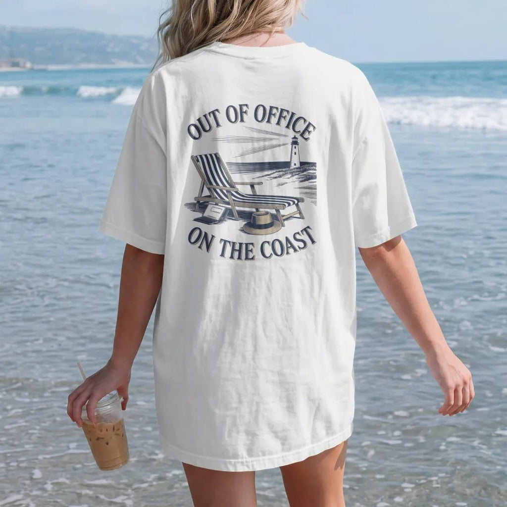 Woman on the beach in a White tee, back view: a striped lounge chair, straw hat and closed laptop on a beach with a lighthouse, under Out Of Office and On The Coast, as a fine engraving in navy and antique gold.