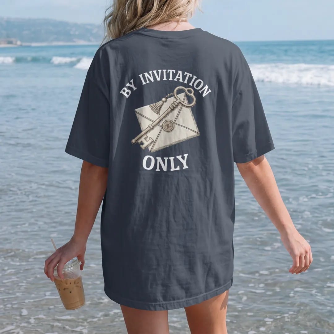 Woman on the beach in a Midnight tee, back view: an ornate tasseled key over a wax-sealed envelope under By Invitation and Only, as a fine engraving in cream and champagne gold.