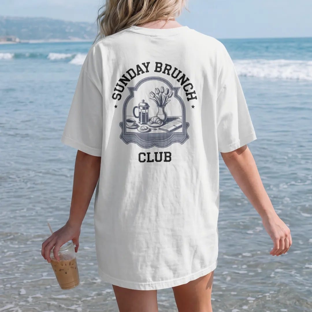 Woman on the beach in a White tee, back view: a brunch table with a French press, croissants, tulips and a newspaper in a scalloped frame, under Sunday Brunch and Club, as a fine engraving in navy and antique gold.