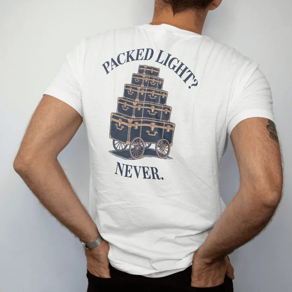 Man wearing a White tee, seen from the back: stacked monogrammed steamer trunks and hatboxes on a luggage cart under Packed Light? and Never., as a fine engraving in navy and antique gold.