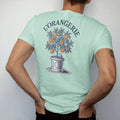 Man wearing a Chalky Mint tee, seen from the back: a potted orange tree with ripe fruit and a small bird in a classic planter box under an arched L'Orangerie, as a fine engraving in navy and antique gold.