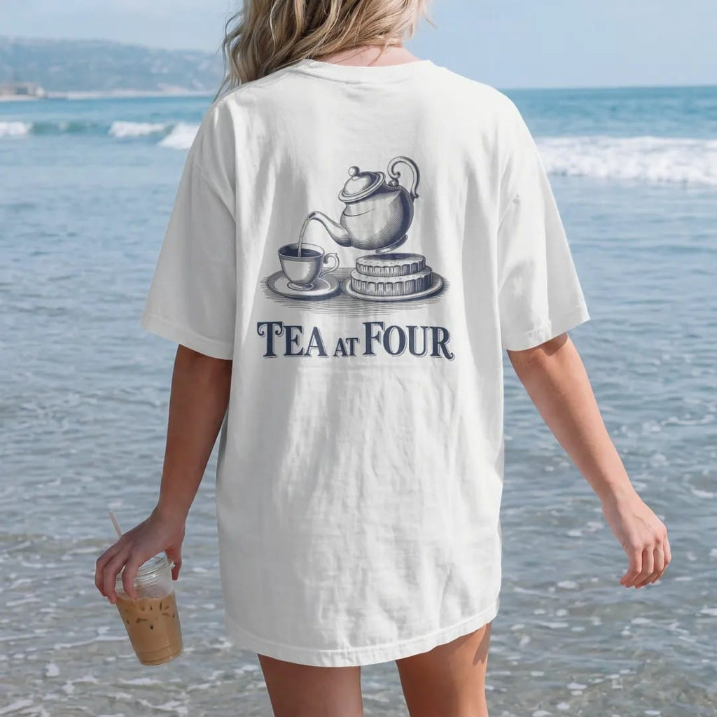 Woman on the beach in a White tee, back view: a porcelain teapot pouring into a cup beside a tiered cake tray with Tea At Four, as a fine engraving in navy and antique gold.