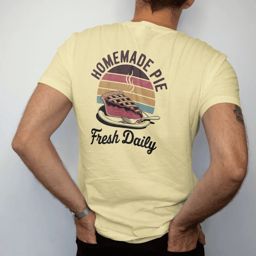 Man wearing a Butter tee, seen from the back: a steaming slice of lattice-top cherry pie on a diner plate, with "HOMEMADE PIE" and "FRESH DAILY" in chunky 70s lettering and brush script, printed in faded, cracked brown, rust red, mustard and dusty…