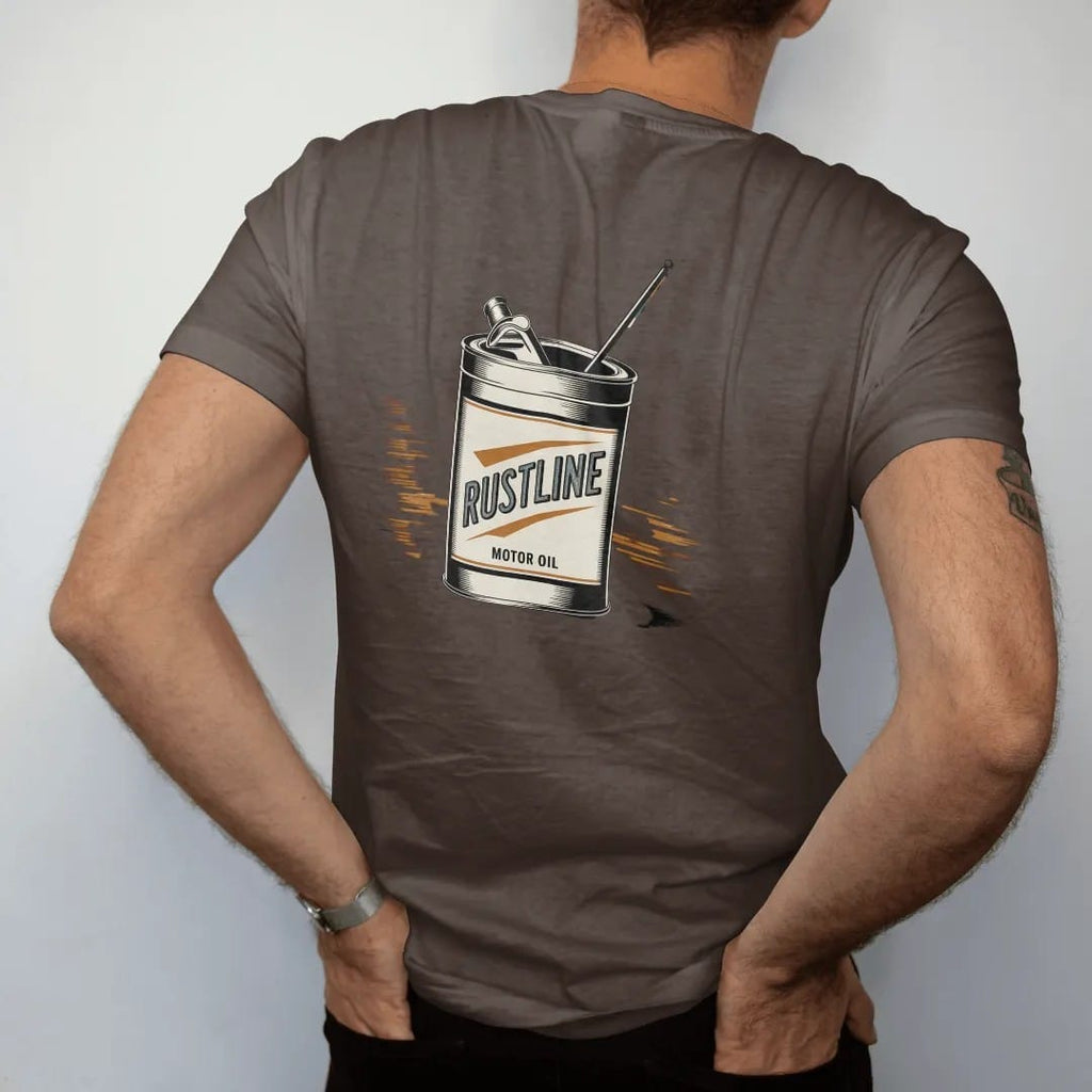 Man wearing a Espresso tee, seen from the back: a dented vintage tin oil can with a racing flag, with "RUSTLINE" and "MOTOR OIL" in chunky 70s lettering and small 70s caps, printed in faded, cracked cream, mustard, burnt orange and dusty teal over…
