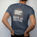 Man wearing a Midnight tee, seen from the back: a drive-in movie screen under stars with vintage car silhouettes, with "DRIVE-IN" and "DOUBLE FEATURE" in chunky 70s lettering and small 70s caps, printed in faded, cracked cream, mustard, burnt…