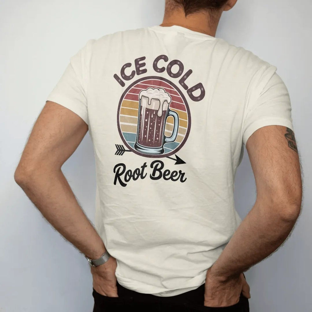 Man wearing a Ivory tee, seen from the back: a frosty root beer mug with spilling foam, with "ICE COLD" and "ROOT BEER" in chunky 70s lettering and brush script, printed in faded, cracked brown, rust red, mustard and dusty teal over faded sunset…